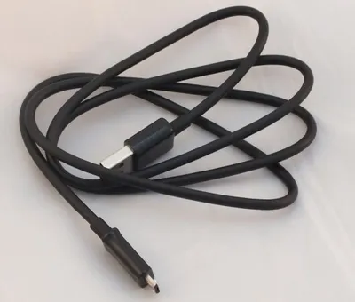 A black USB cable is coiled on a white surface.