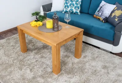 A wooden coffee table is placed on a fluffy rug in front of a blue sofa with decorative pillows.