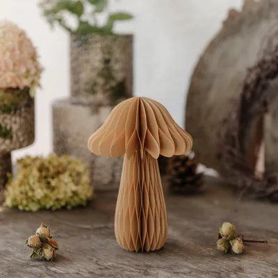 A decorative paper mushroom sits on a wooden surface, surrounded by natural elements like dried flowers and nuts.