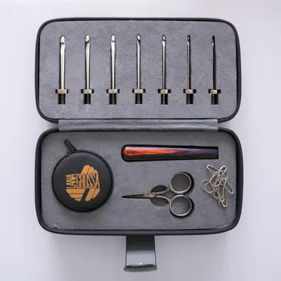 A crochet hook set is neatly arranged in a case, with accessories like scissors and paper clips also included.