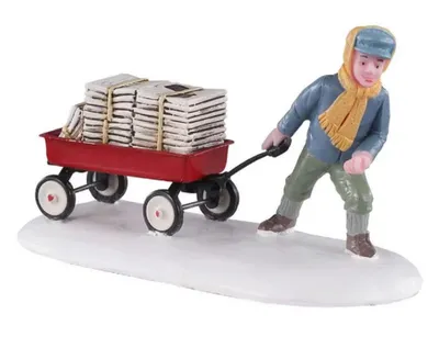 Miniaturfigur eines Jungen, der im Schnee einen roten Wagen zieht, der mit Zeitungen beladen ist.