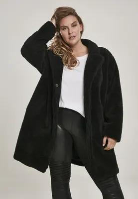 A woman is posing in a studio setting, wearing a black faux fur coat.