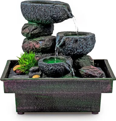 A tabletop water fountain with multiple tiers of stacked stones and bowls, with water flowing between them. It is set against a white background.
