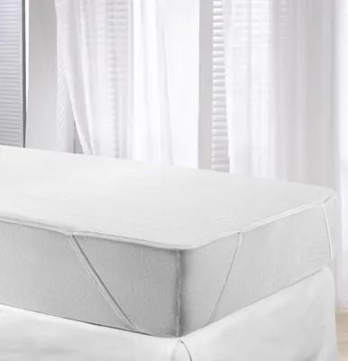 A white mattress protector is shown on a bed, with sheer white curtains in the background.