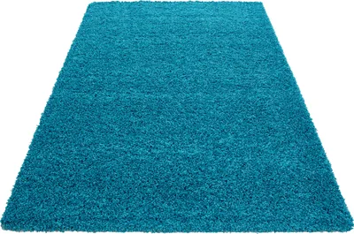 A high-pile, turquoise rug is shown from a diagonal, slightly elevated angle against a white background.
