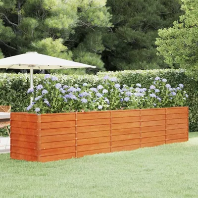 A wooden planter box filled with purple flowers in a garden setting, with a patio umbrella in the background.