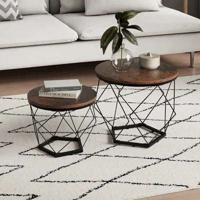 Two nesting coffee tables with wooden tops and geometric metal bases are placed on a rug in front of a sofa.