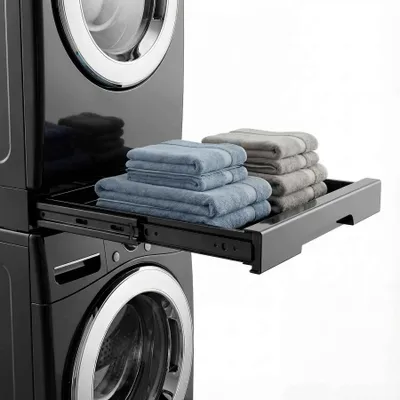 A close-up view of a black washing machine with a pull-out shelf holding folded towels.