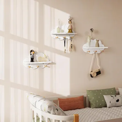 Three cloud-shaped shelves with hooks mounted on a light beige wall above a crib.