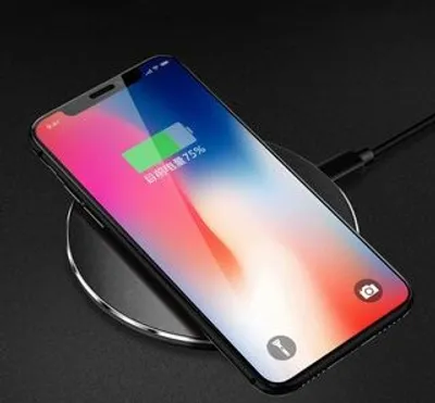 A smartphone is placed on a wireless charging pad, displaying its battery status.