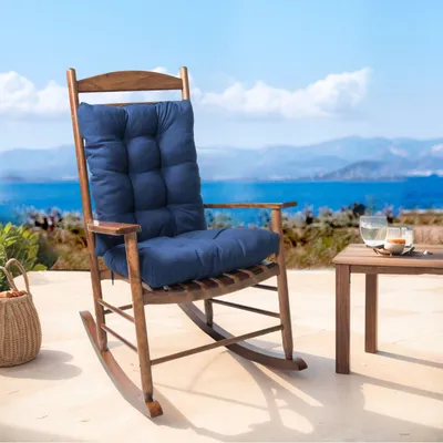 A rocking chair with a dark blue cushion sits on a patio overlooking a body of water and mountains.