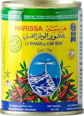 A close-up of a can of Harissa paste, decorated with chili peppers and a lighthouse illustration.