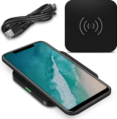 A smartphone is placed on a wireless charging pad, with a USB cable and the charging pad itself also visible.