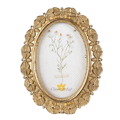 A gold-colored oval picture frame with a floral design and a picture of a plant inside.