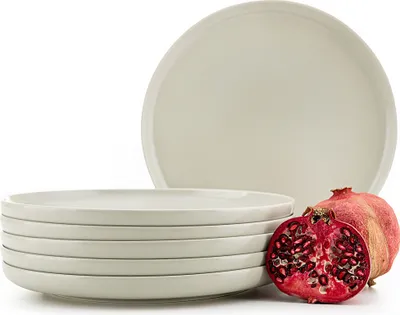 A stack of beige plates with a halved pomegranate next to them.