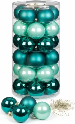 A clear, professional studio shot of a cylinder of Christmas ornaments in various shades of green and teal, with some loose ornaments and hooks in the foreground.