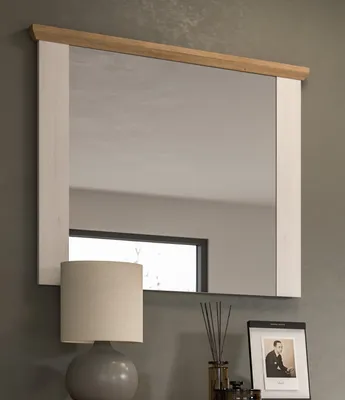 A mirror with a white and wood frame is displayed on a gray wall above a table with a lamp and a framed photo.