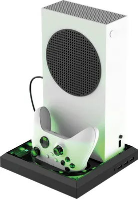 A white Xbox Series S console is shown vertically on a black docking station with a white controller in front of it. The docking station has green LED lighting.