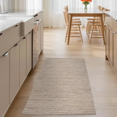 A kitchen with a rug in front of cabinets and a dining table in the background.