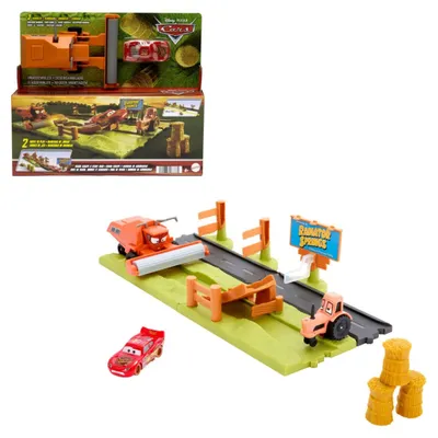 A toy playset featuring characters and vehicles from Disney Pixar's Cars franchise, set in a farm-like environment with a road, fences, a combine harvester, a tractor, and hay bales.