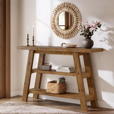 A wooden console table with shelves, decorated with a mirror, vase, books, and basket.