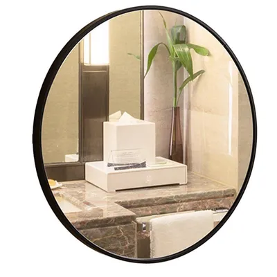 A round mirror reflecting a bathroom counter with a tissue box, a vase with a plant, and a towel.