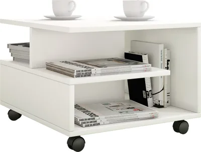 A white coffee table with two shelves, holding magazines and books, and two cups on top. The table has wheels.