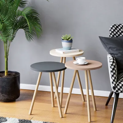 A set of three nesting side tables with a plant and a cup of coffee on them, next to a chair.