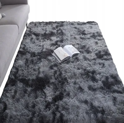 A dark gray shaggy rug is shown in a room, with a portion of a gray sofa visible on the left. An open book lies on the rug.