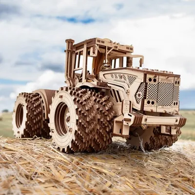 A wooden model tractor sits on a bed of straw, with a cloudy sky in the background.