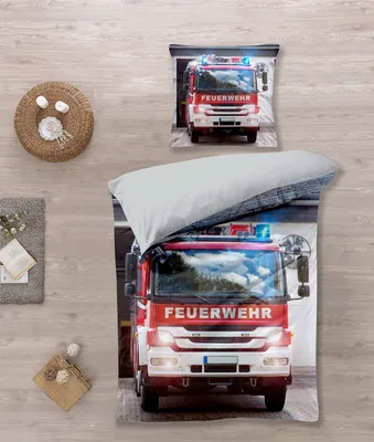 A bedding set with a fire truck design is laid out on a wooden floor.