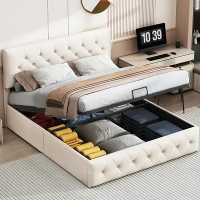 A storage bed with its storage compartment open, revealing folded linens and other items. A desk with a computer is visible in the background.