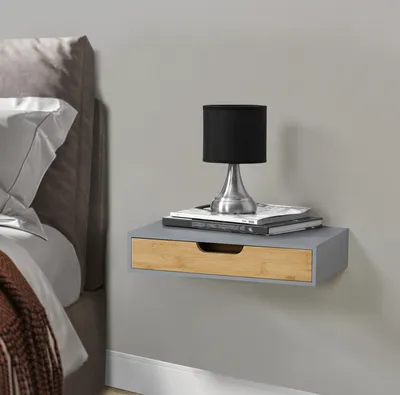 A floating shelf with a drawer is mounted on a gray wall next to a bed.
