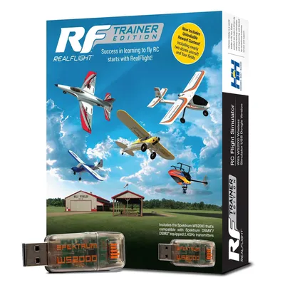 The image shows the box of a RealFlight Trainer Edition RC Flight Simulator, with various RC aircraft depicted in flight against a blue sky with clouds. Two USB dongles are also shown in the foreground.