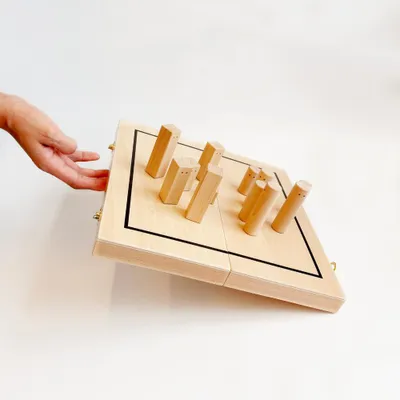 A hand is shown reaching towards a wooden game board with several wooden pieces on it. The board is tilted, showing its side and top.