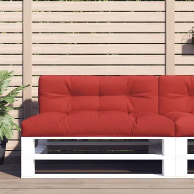 A red cushion on a white pallet sofa base, set against a slatted wooden fence.