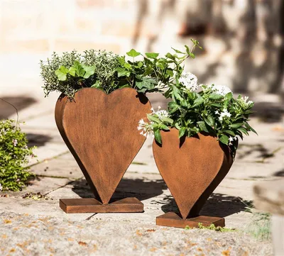 Two heart-shaped metal planters with plants in them, placed on a stone patio.