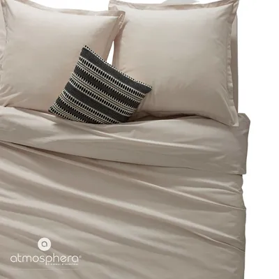 A close-up view of a bed with beige bedding and a decorative pillow.