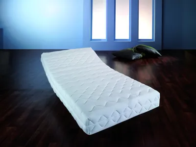 A white mattress is placed on a dark wooden floor in a room with blue walls and three tall windows.