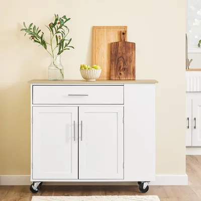 A white kitchen island with a wood-effect countertop is shown against a light yellow wall. Decorative items like a vase with greenery, a bowl of fruit, and cutting boards are placed on top.