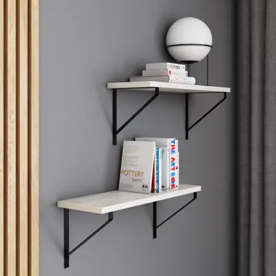 Two white shelves with black brackets mounted on a gray wall, decorated with books and a lamp.