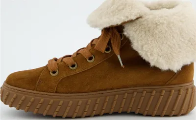A side view of a brown suede high-top sneaker with a cream-colored fluffy lining and a thick brown sole.