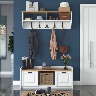 An entryway bench with a shelf and coat hooks, decorated with hanging coats, bags, a hat, and decorative items.