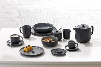 A table setting with a dark gray dinnerware set, including plates, bowls, cups, and a teapot.