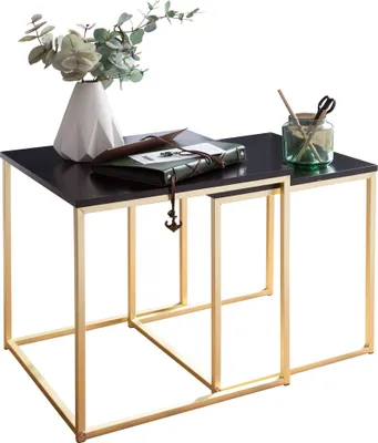 Two nesting tables with black tops and gold metal frames, decorated with a vase of greenery, a book, and scissors in a jar.