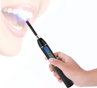 A hand holding a dental curing light device, with the light beam directed at teeth.