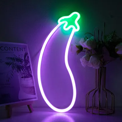 A neon eggplant light is displayed on a surface with a book and a vase of flowers in the background.