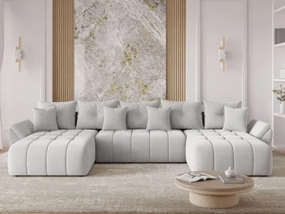 A modern, light gray U-shaped sectional sofa is arranged in a living room setting, facing a coffee table. The sofa is adorned with several matching throw pillows. Behind the sofa, a large abstract artwork with marble-like textures is displayed on a wall wi