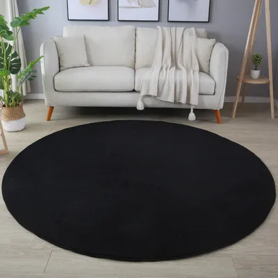 A black round rug in a living room setting with a sofa and plants.