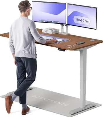 A man stands at a height-adjustable desk with two monitors, using a standing mat.
